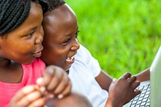 Close up face shot of African kids laughing at scene on laptop outdoors.