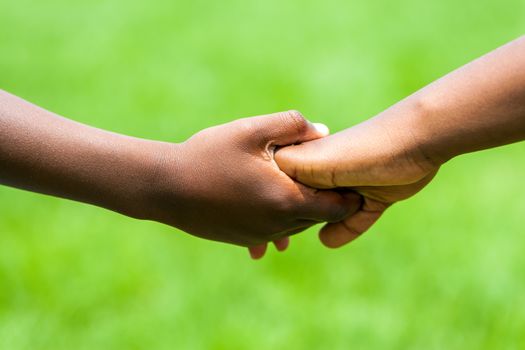 Extreme close up detail of African kids holding hands against green outdoor background.