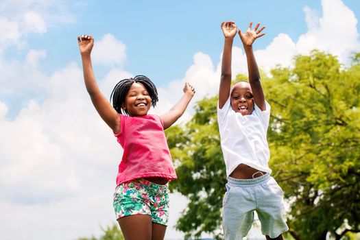 Action portrait of young African boy and girl jumping in park.