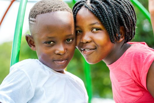 Close up portrait of little African brother and sister joining heads outdoors in park.