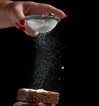 square baked brownie chocolate cake slices sprinkled with white sugar from an iron sieve, small particles fly down, low key