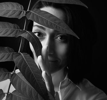 portrait of a beautiful adult woman with short black hair of a Caucasian appearance dressed in a white shirt holds a branch with leaves, black background, black and white tinting