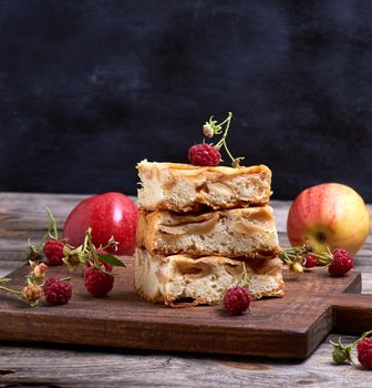 square pieces of apple pie are stacked on a brown wooden board, sponge cake