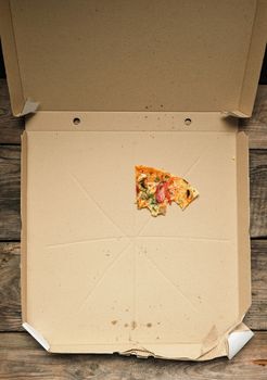 bite of pizza with smoked sausages, mushrooms, cheese and tomatoes in an open brown cardboard box, top view