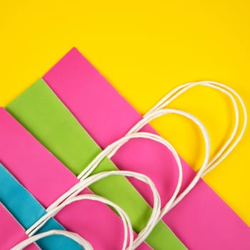 rectangular multi-colored paper shopping bags with white handles on a yellow background, flat lay