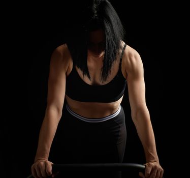 young beautiful athletic girl with muscles in a black bra is wrung out in her arms, doing fitness and sports, studio photo in a low key