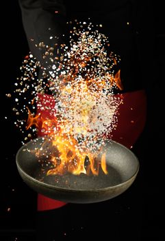 chef holds a round pan and throws the mixture of spices and white salt up, low key