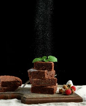 stack of square baked brownie chocolate cake slices sprinkled with white sugar, small particles fly down, low key