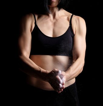 young girl with a sports figure dressed in a black top claps in her hands with white magnesia, preparing before exercise, low key