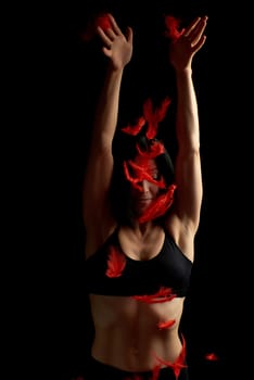 young beautiful athletic girl in black clothes throws up red feathers, arms raised up, low key