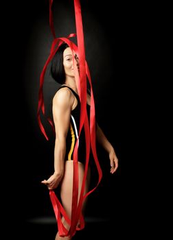 young woman gymnast of Caucasian appearance with black hair spins red satin ribbons, gymnastic exercises on black background