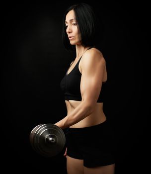 young woman of Caucasian appearance holds steel type-setting dumbbells in her hands, sports training, dark background