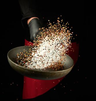 chef holds a round pan and throws the mixture of spices and white salt up, low key