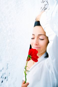 portrait of a young woman with a red rose in her hands surrounded by lace white curtains, waking up in the early morning