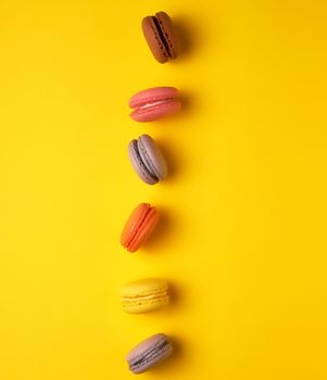 assortment of multi-colored baked round macarons on a yellow background, flat lay, copy space 