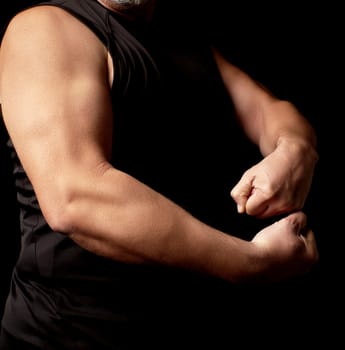 adult man with a sports figure in black clothes strained his muscles in his arms, bodybuilder shows his biceps, a low key