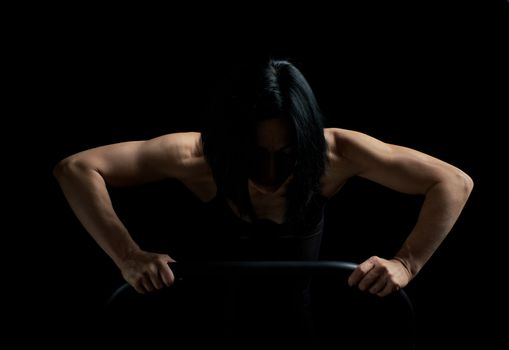 young girl of athletic appearance with black hair is pushing up from the surface on a dark background, athlete’s muscular body is tense