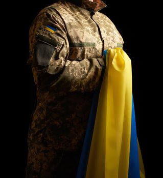 Ukrainian soldier holds in his hand the yellow-blue flag of the state, he pressed his hand to his chest, concept of the memory of the dead soldiers