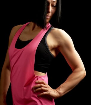young girl with black hair dressed in pink sportswear posing on a dark background, look down