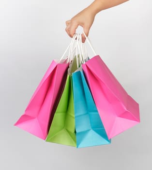 female hand holding four colored paper shopping packaging bags on white background, concept of seasonal sales