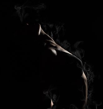young beautiful athletic girl with muscles in a black bra bent the body back, white smoke vapor envelops the body
