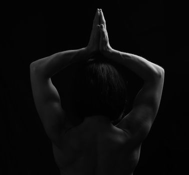 young girl of athletic appearance with black hair raised her hands up and joined her palms, vrikshasana pose, view from the back, low key
