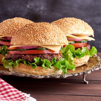 burger with fried cutlet, cheese and vegetables in a round wheat flour bun on an iron plate, close up