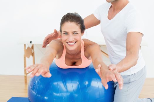 Physical therapist assisting young woman with yoga ball in the gym at hospital
