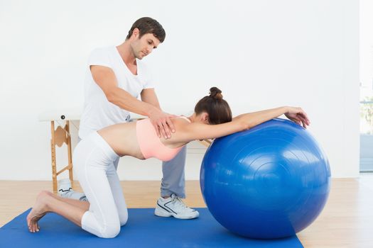 Physical therapist assisting young woman with yoga ball in the gym at hospital