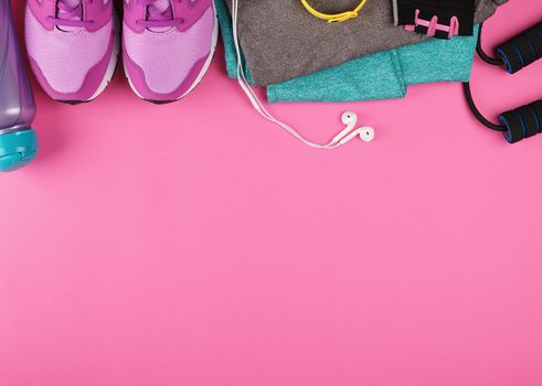 pink women's sneakers, a bottle of water, gloves and a jump rope for sports on a pink background, top view, copy space, flat lay