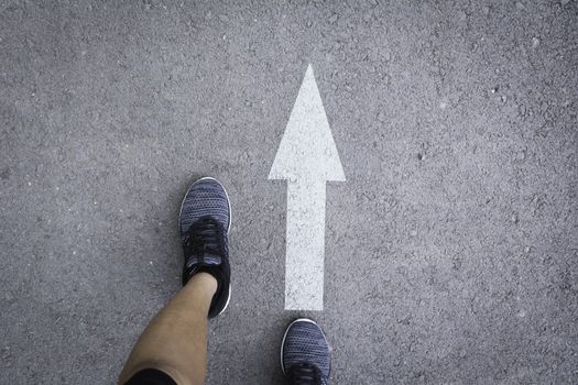 Top view of man wearing shoes choosing a way marked with white arrows. Chooses the right path concept.