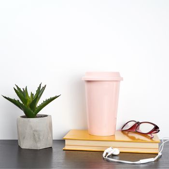 closed book and pink ceramic glass with coffee on a black table, white wall