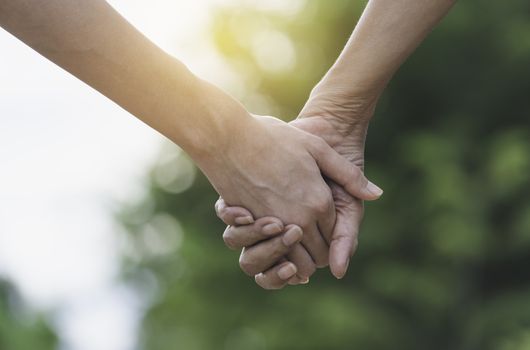 Hand of lady and younger lady holding together on blur background