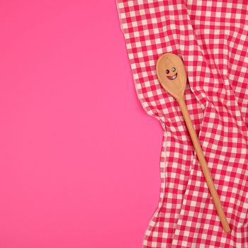 wooden spoon with a carved face on a red kitchen towel, pink background, copy space