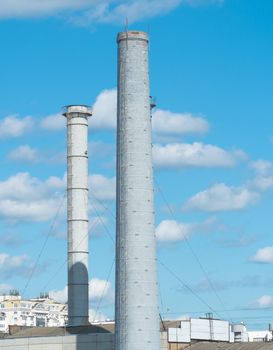 Pipes of an industrial enterprise against a blue sky with clouds. Chimney without smoke