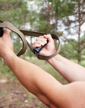 athlete does sports strength exercises on belts, outdoor fitness, close up