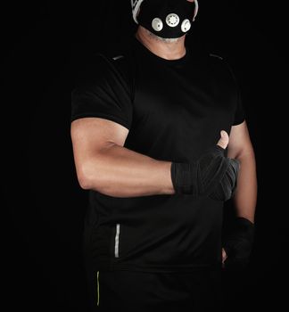 athlete in black uniform, training mask and hands wrapped in black bandage stands and shows a hand gesture like, black background