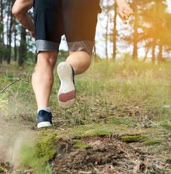 adult man in black shorts runs in the coniferous forest against the bright sun, concept of a healthy lifestyle and running in the fresh air, back view