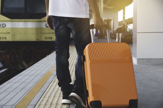 Man dragging orange suitcase luggage bag, walking in train station. Travel concept.