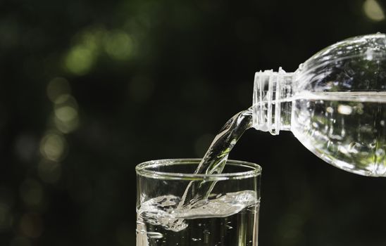 Pouring water from bottle into the glass on blurred background.
