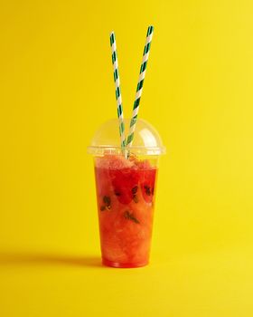 smoothie from ripe red watermelon in a plastic cup,  two paper tubes  on a yellow background