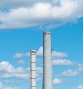 Pipes of an industrial enterprise against a blue sky with clouds. Chimney without smoke