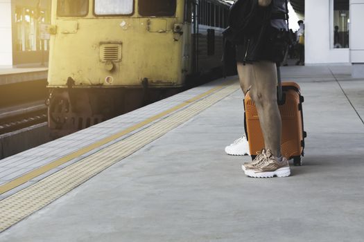 Woman dragging orange suitcase luggage bag, walking in train station. Travel concept.