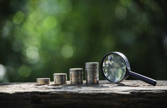 Saving money concept with money coin stack and magnifying glass. Financial and accounting concept.