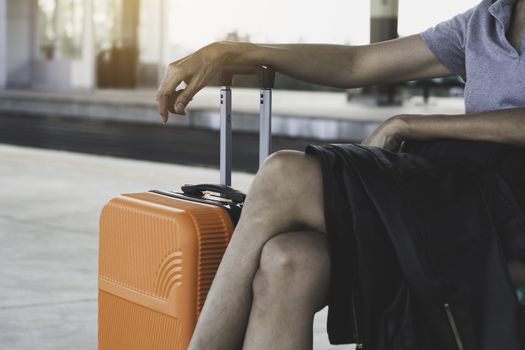 Woman with orange suitcase luggage bag, sitting in train station. Travel concept.