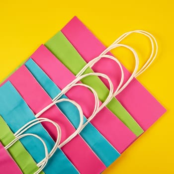 multi-colored paper shopping bags with white handles on a yellow background, flat lay