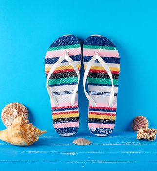  pair of multi-colored rubber slippers on a blue background, near seashells, background for travel and leisure