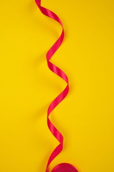 twisted red silk ribbon, yellow background, top view, copy space, holiday background