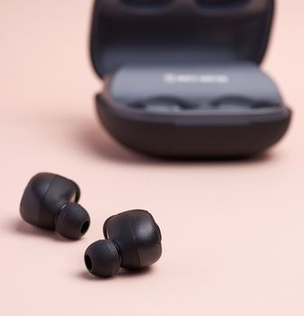 black wireless little earphones and a charging box on a beige  background