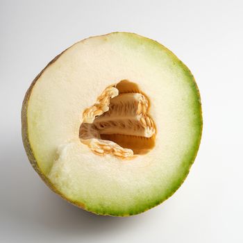 half of ripe yellow melon with seeds on white background, close up